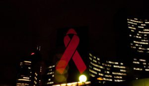 a red AID-awareness ribbon projected on the United Nations buildings at night
