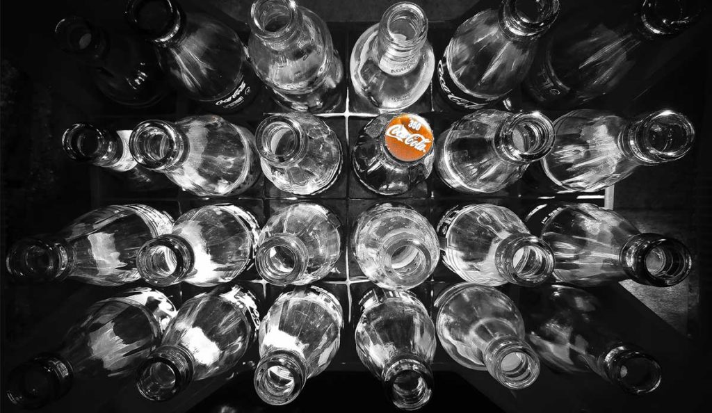A case of glass soda bottles, one with a red Coca-Cola cap