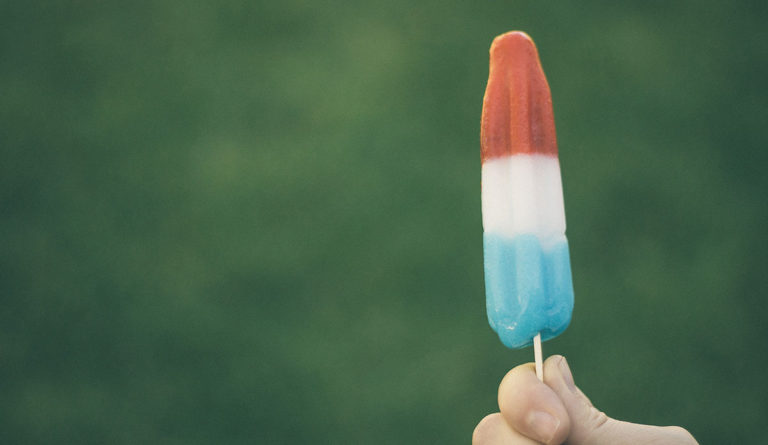 a hand holding a red white and blue popsicle
