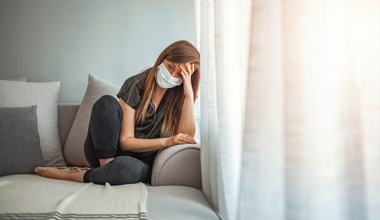 a woman sitting on a couch wearing a face mask