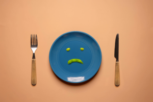 a blue plate with a sad face on it next to a fork and knife