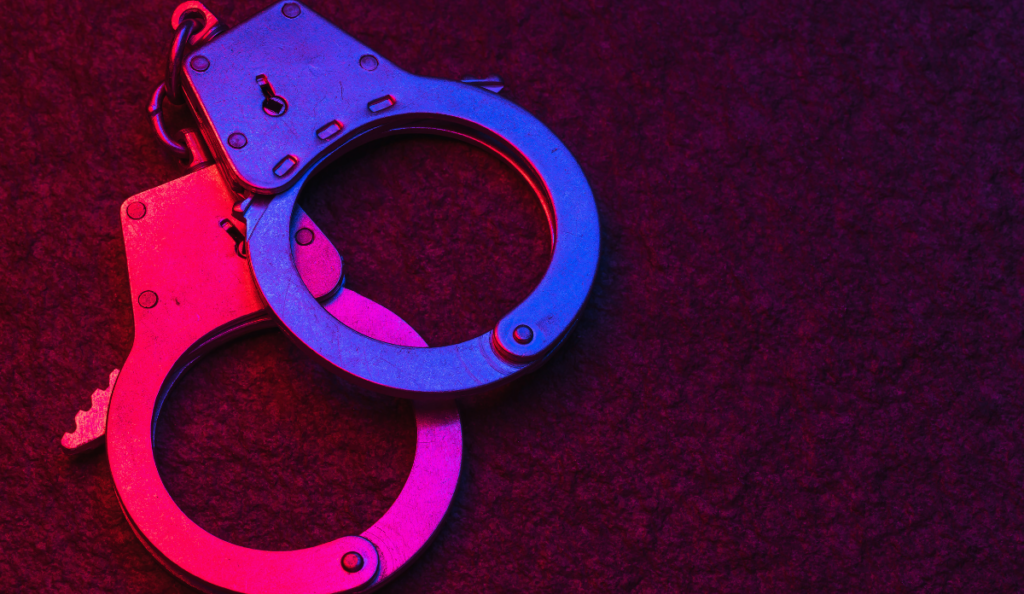 Handcuffs on dark background illuminated by flashing lights of police car, signifying arrest