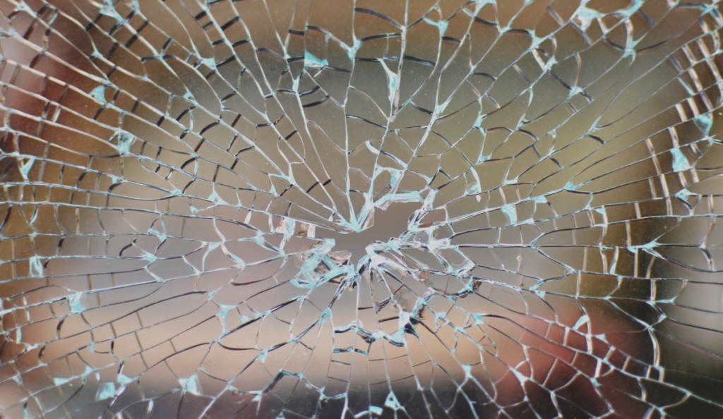 Broken window with cracked glass pattern and a bullet hole in the middle, representing gun violence