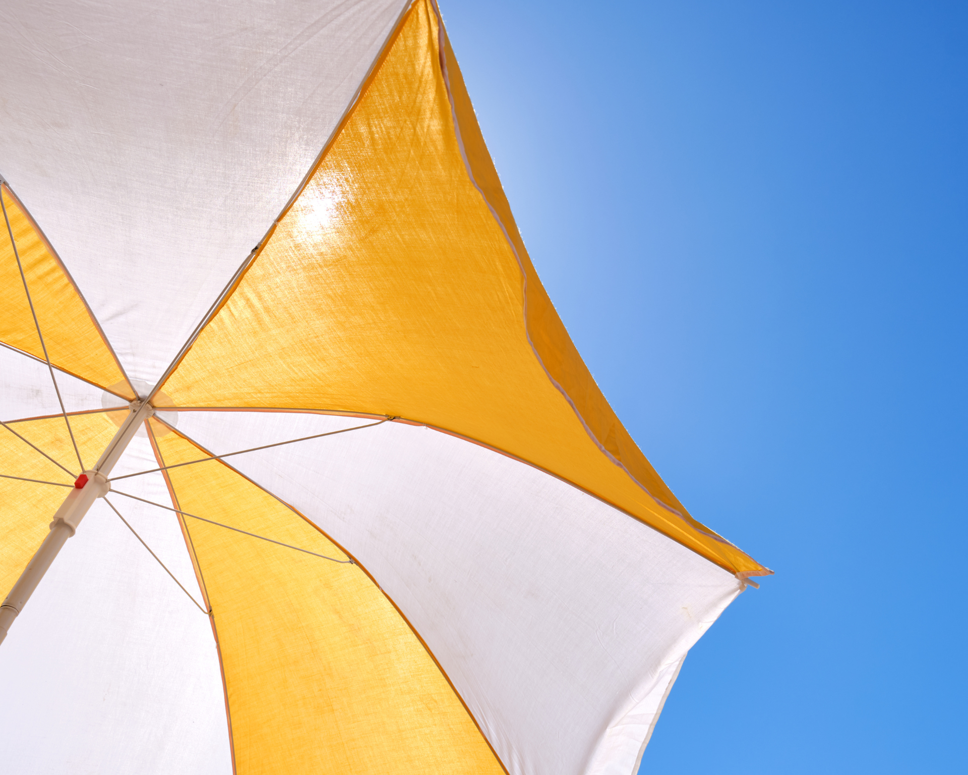 Yellow and white umbrella on a blue sky for protection from the sun on the beach