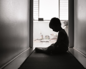 Young child sitting alone in a dark hallway