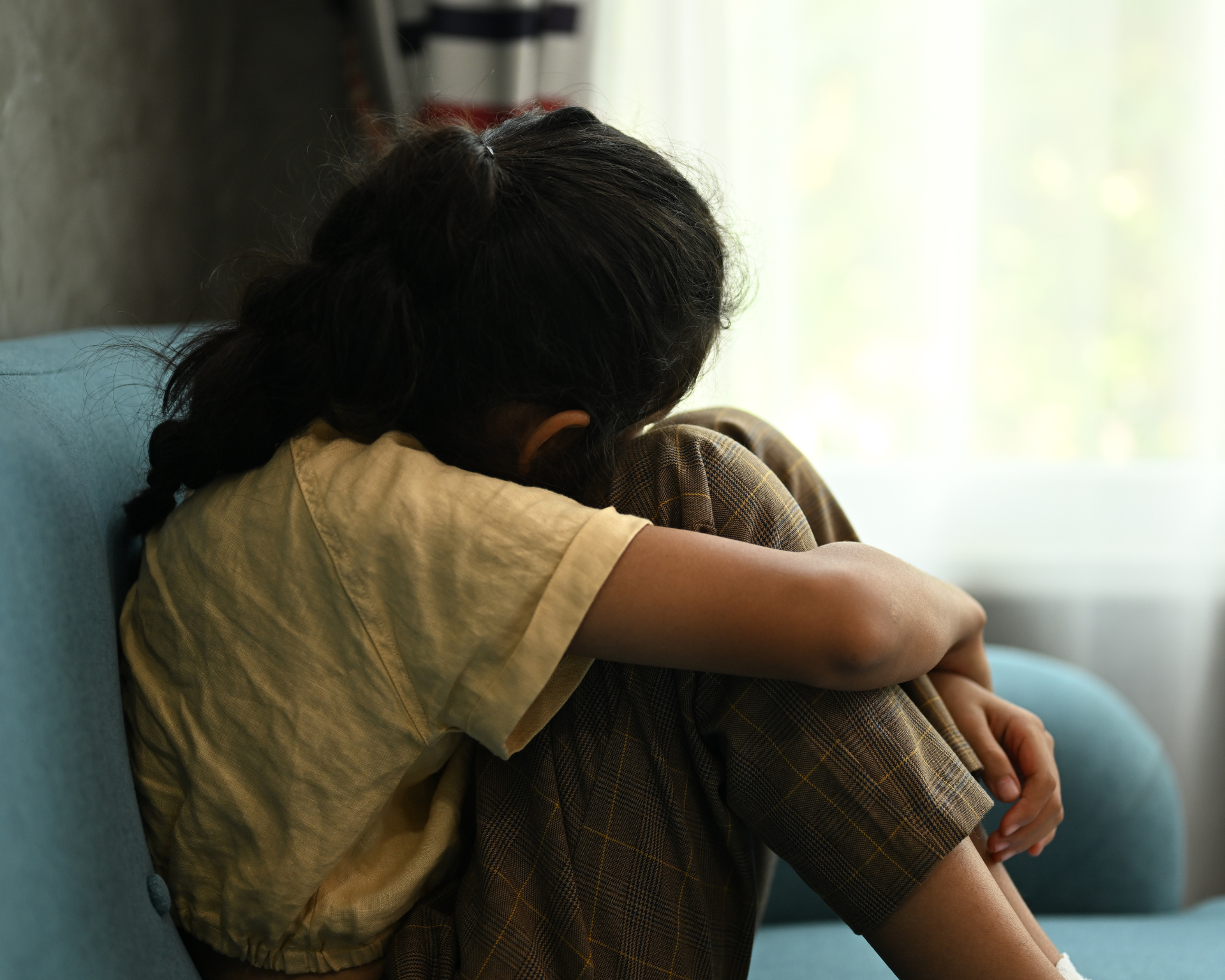 Young, sad girl sitting on couch with face turned away. Child mental health concept