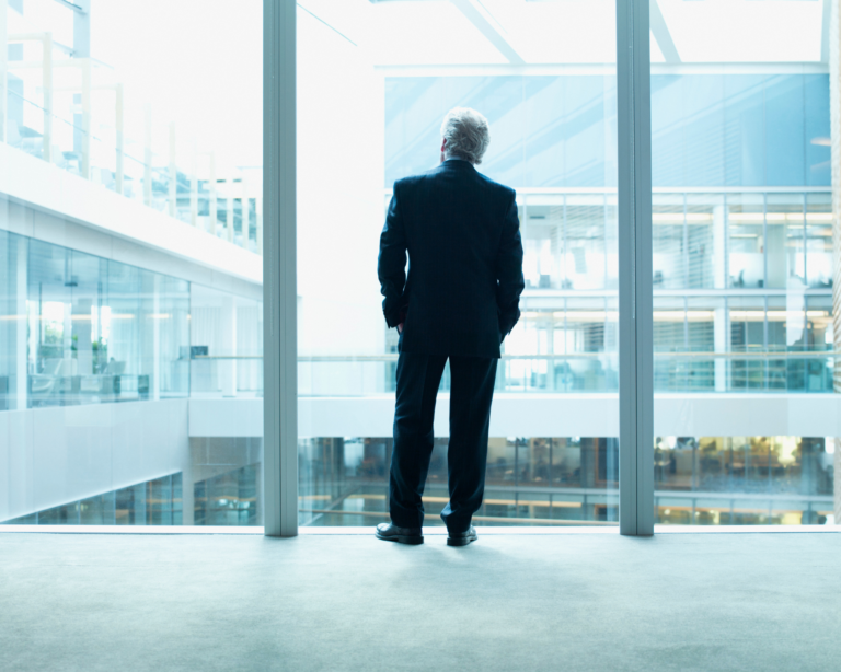 older businessman looking out glass wall of office