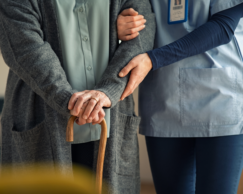 older dementia patient with cane being guided by a health care worker in a nursing home