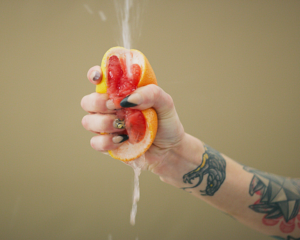 femme hand squeezing a grapefruit, causing the juices to squirt