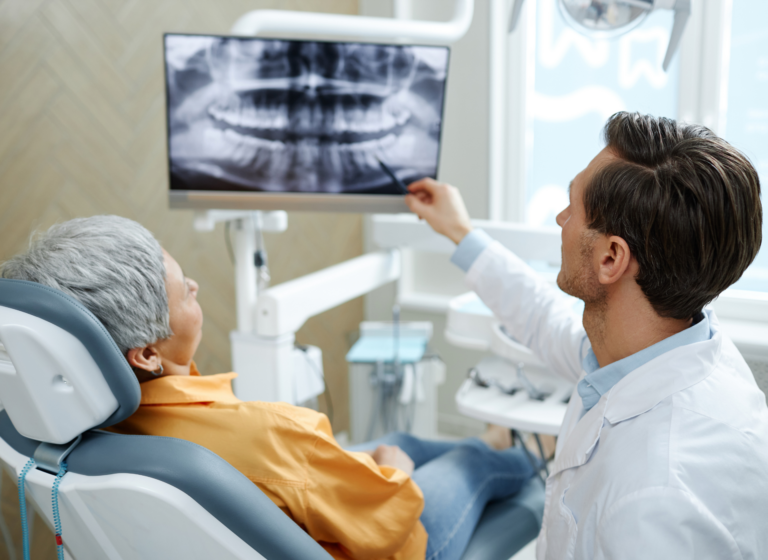 Back view of male dentist pointing at tooth X-ray image on screen during consultation in a dental clinic