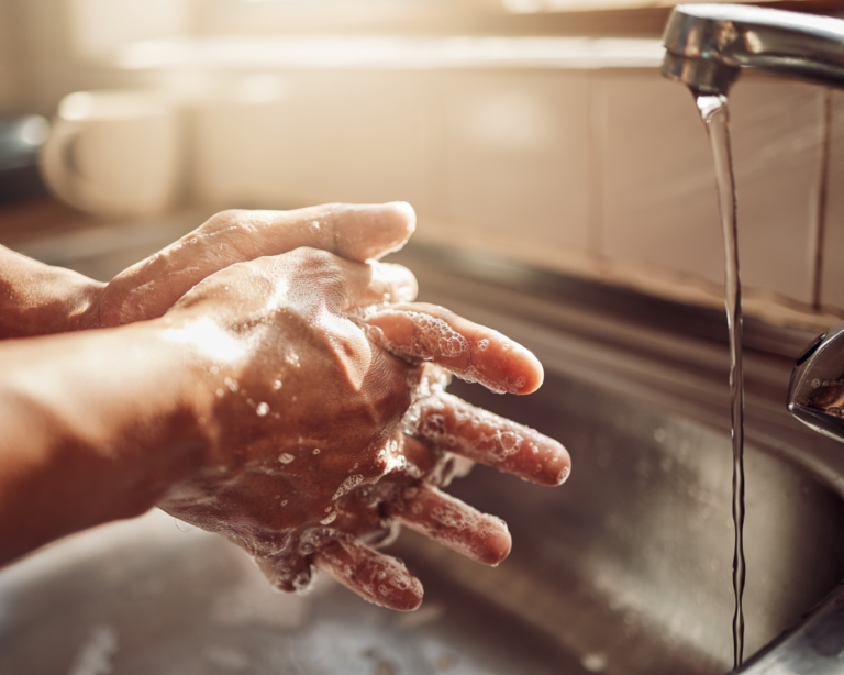 Shot of an unrecognisable man washing his hands in the kitchen sink at home