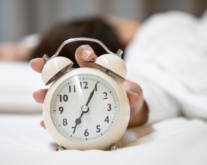 woman hitting snooze on alarm clock