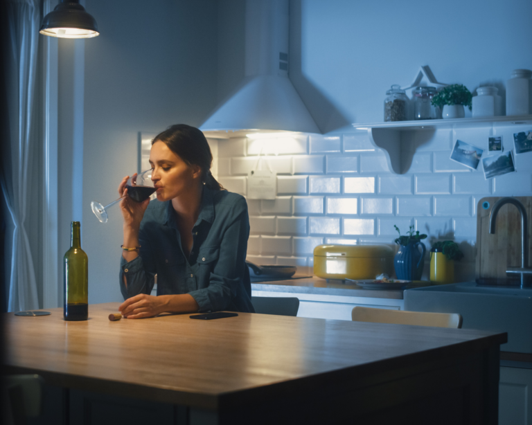 Portrait of a young woman sitting along in a kitchen and drinking a glass of wine