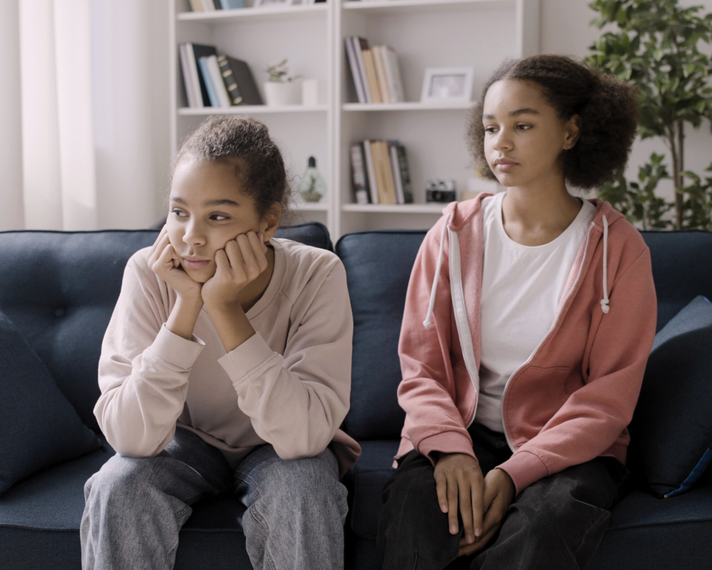 Portrait of two young, sad women sitting on a couch. Sibling trauma concept