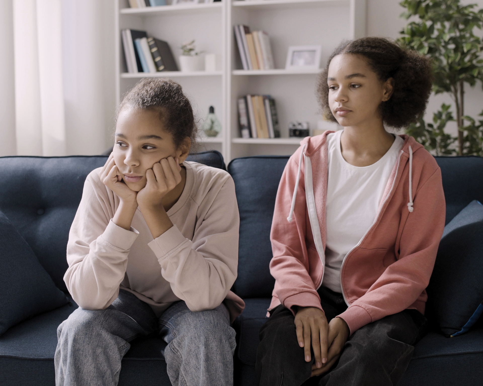 Portrait of two young, sad women sitting on a couch. Sibling trauma concept