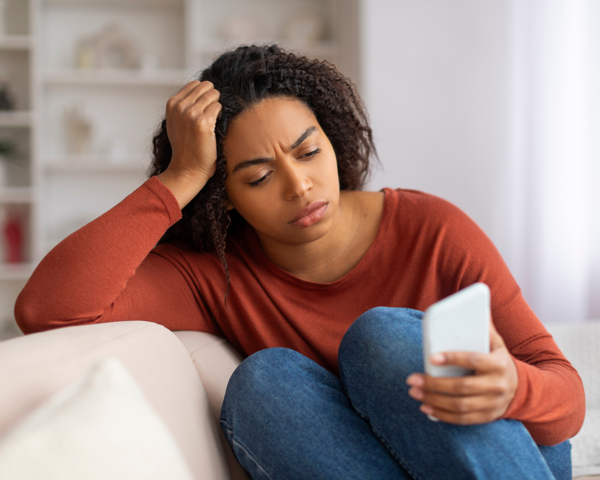 portrait of a young, distressed Black woman looking at phone and scrolling on social media