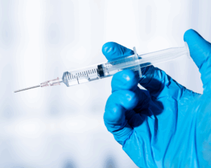 Syringe in gloved hand on white background. Vaccination concept