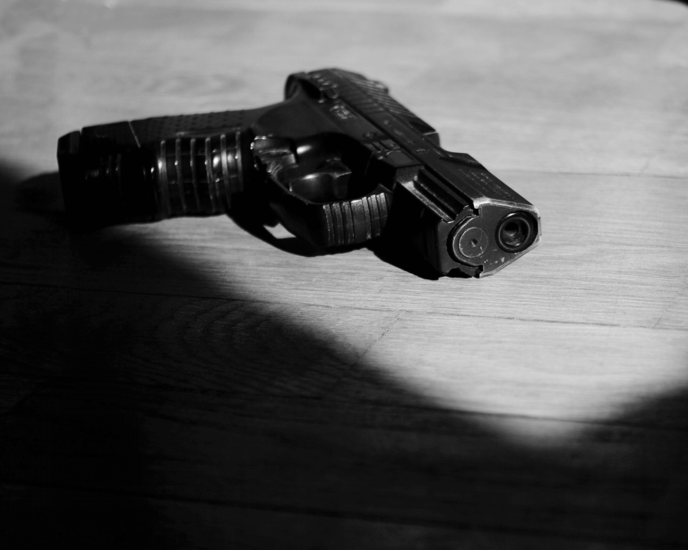close-up image of a gun lying on a table with harsh shadows