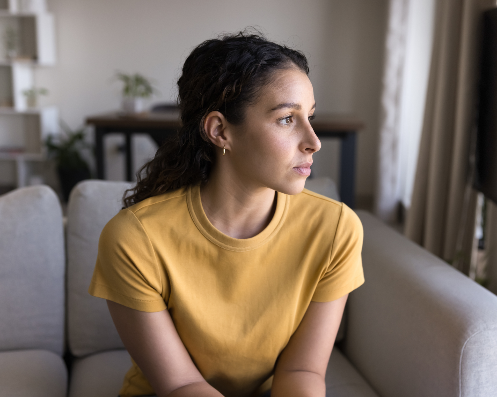 Portrait of a young woman sitting on a couch and looking out the window. Mental health and women's health concept