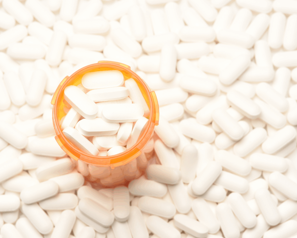 Opioid crisis concept. High-angle view of a prescription bottle filled with pills surrounded by more of the same tablets