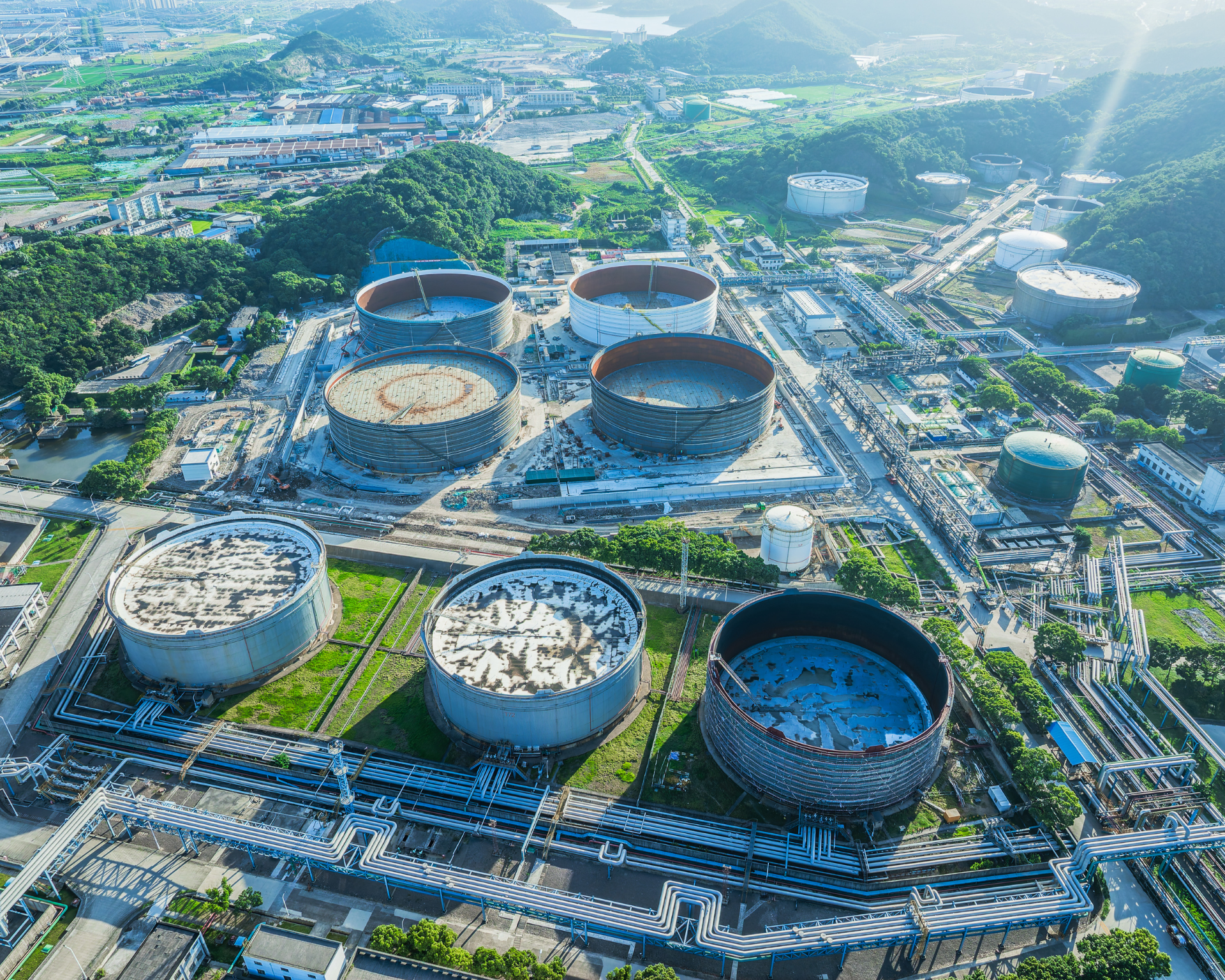 Large crude oil storage tanks beneath an oil refinery in a green hilly area