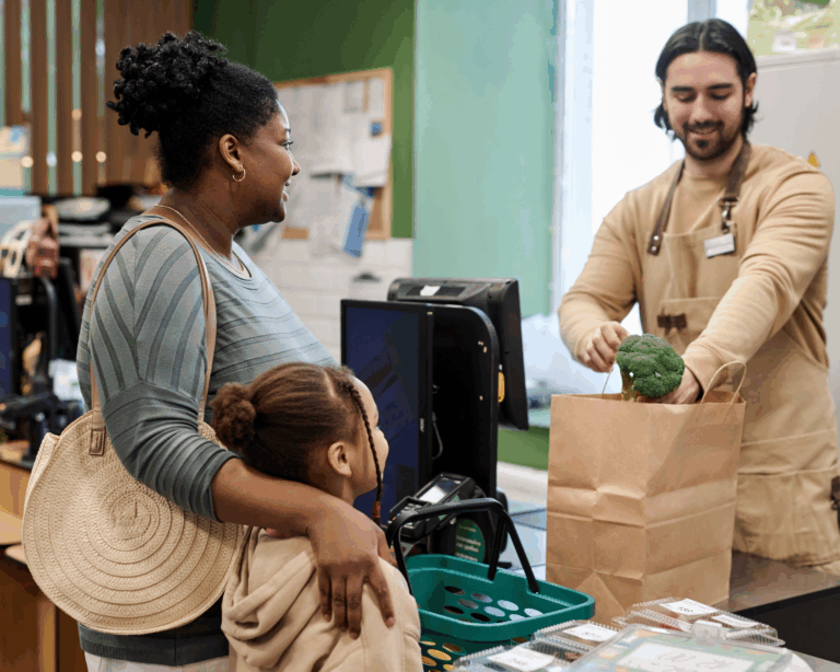 Portrait of male cashier in supermarket helping young mother with groceries and packing vegetables into a paper bag. WIC benefits concept