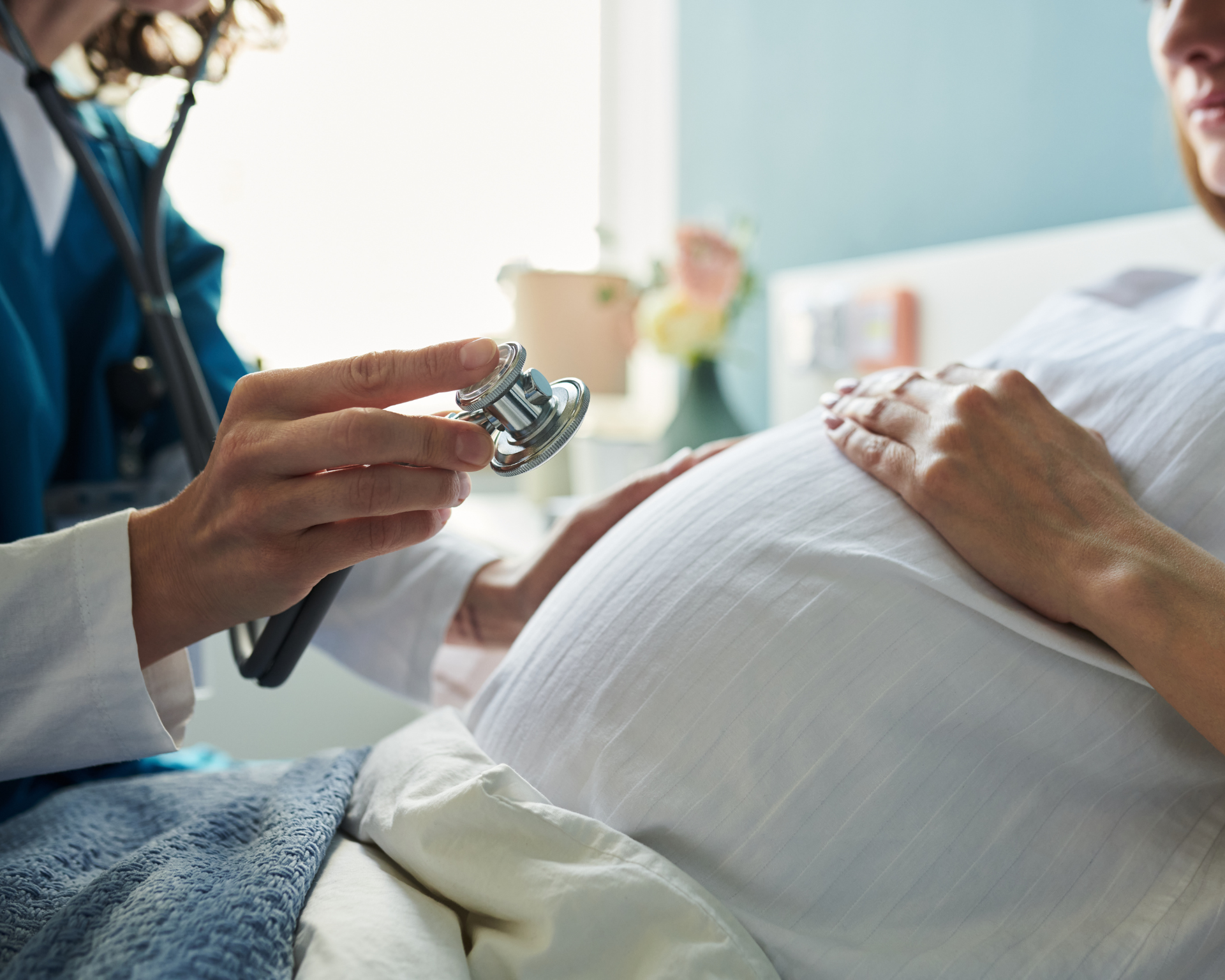 Close up of a pregnant woman sitting during medical examination with female doctor holding stethoscope near belly, focusing on prenatal health care and pregnancy monitoring