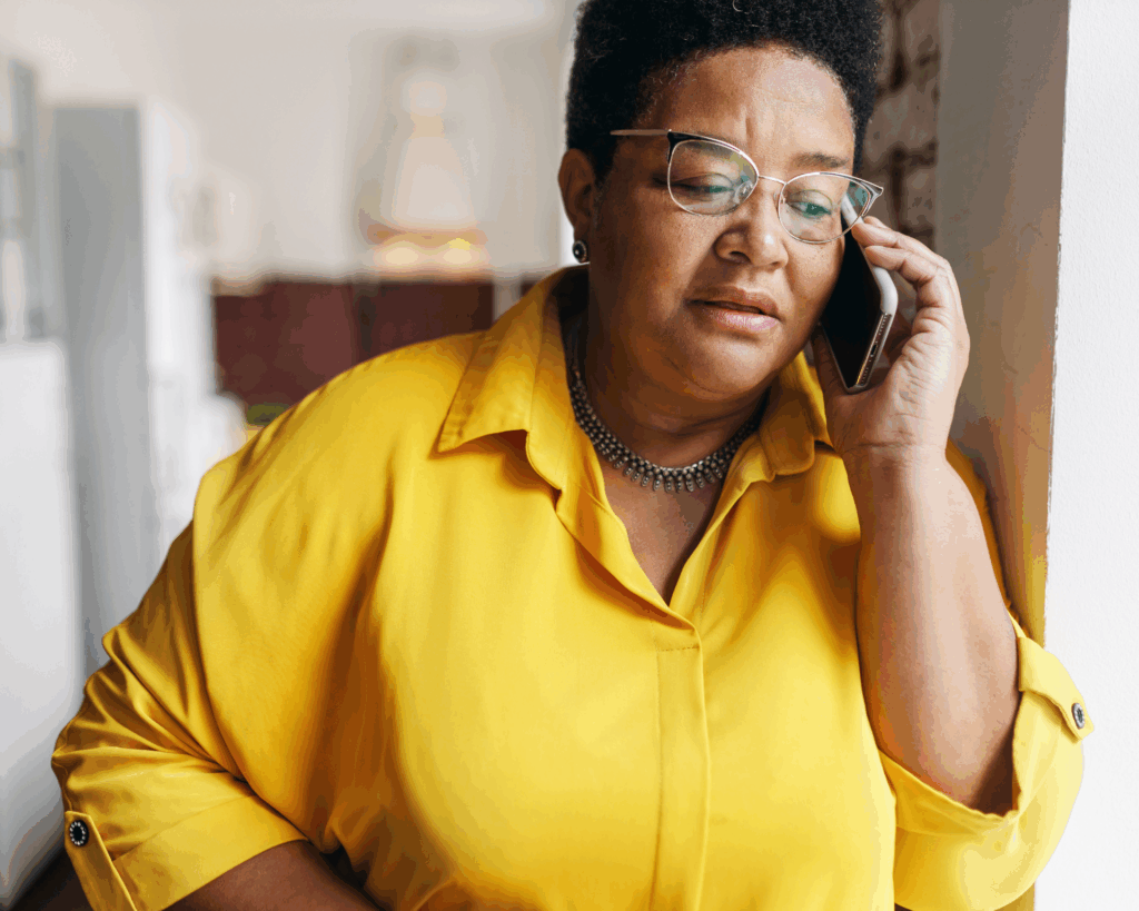 Portrait of an older Black woman in yellow shirt leaning against the wall and talking on the phone