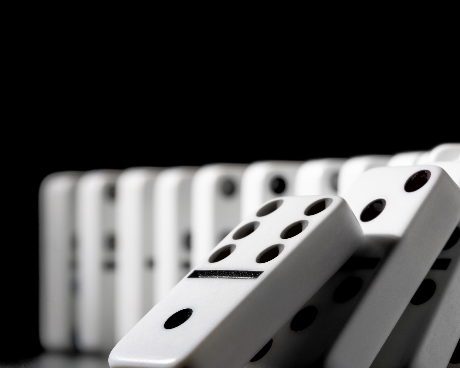 Domino pieces put in a row and starting to fall on a black background. Visual representation of title, "Depression's Domino Effect"