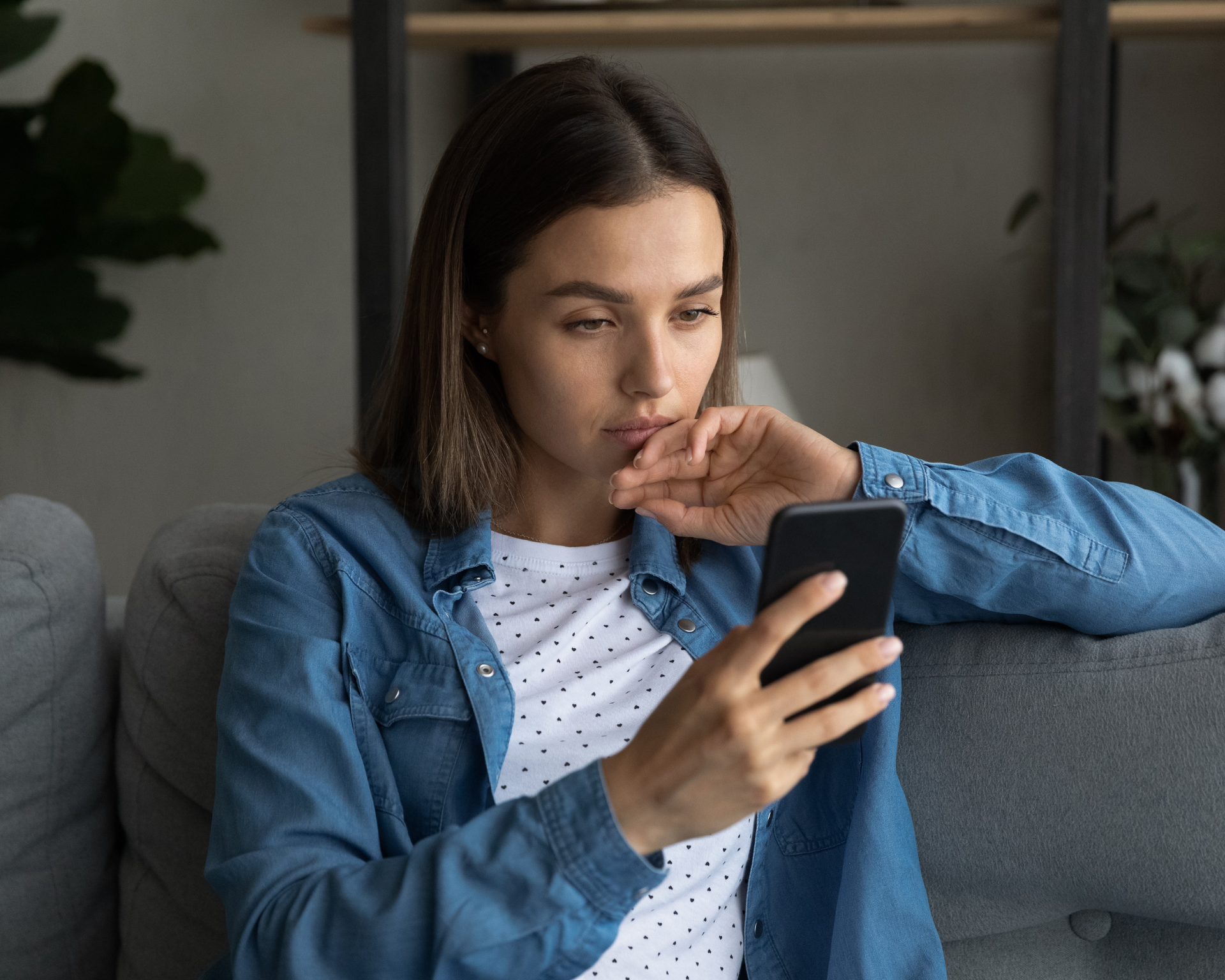 Portrait of a serious woman sitting on a couch and looking at her phone. Telehealth concept