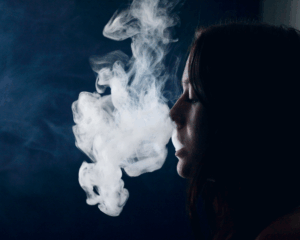 Side view of a teenager smoking cannabis in front of a black background