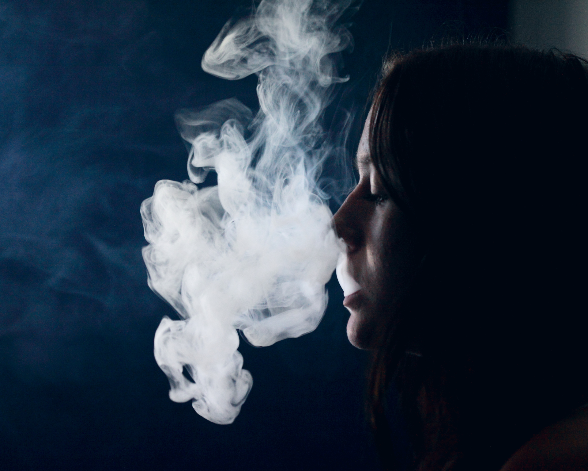 Side view of a teenager smoking cannabis in front of a black background