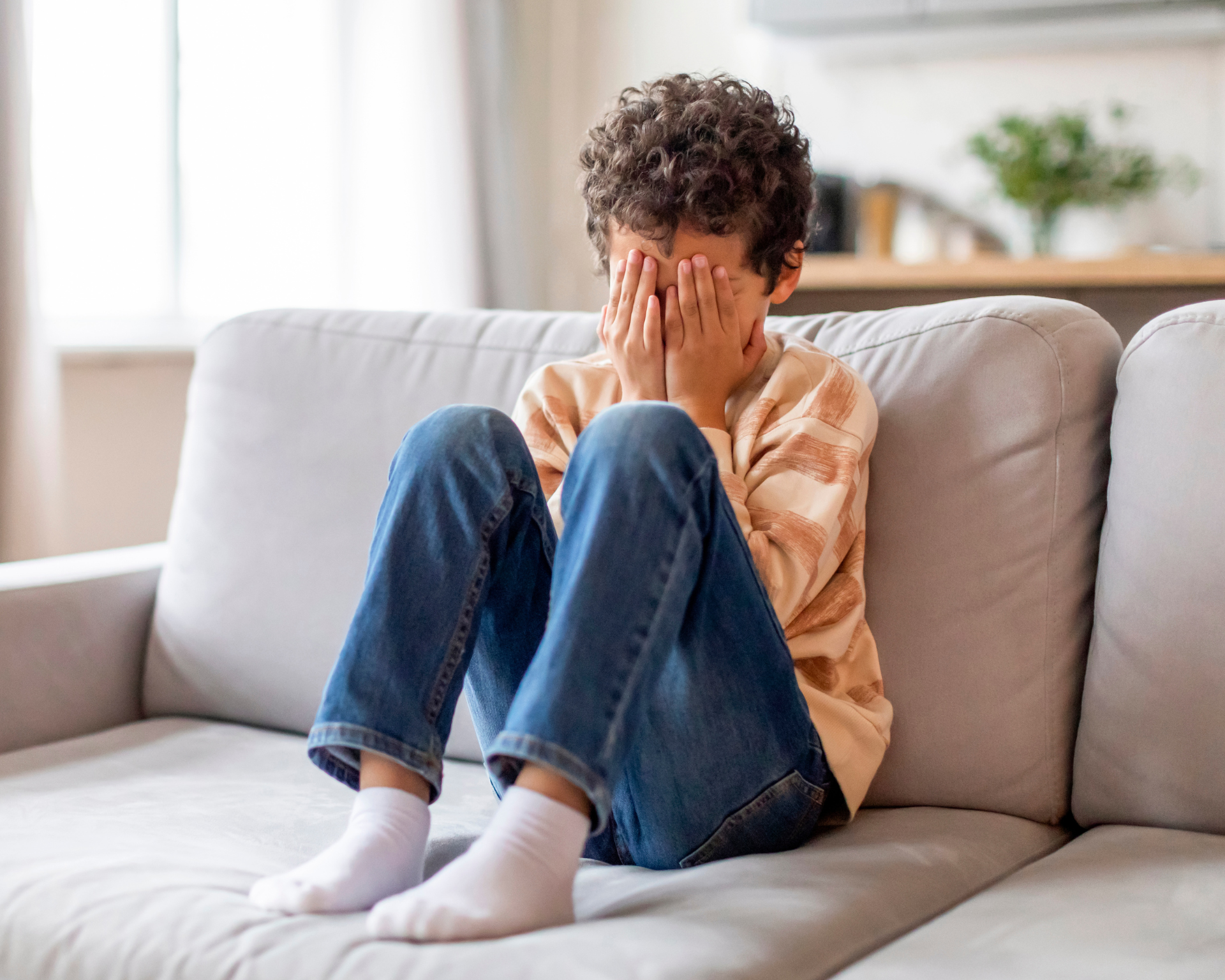 Young boy sitting on couch with face in hands, upset. Behavioral challenges concept