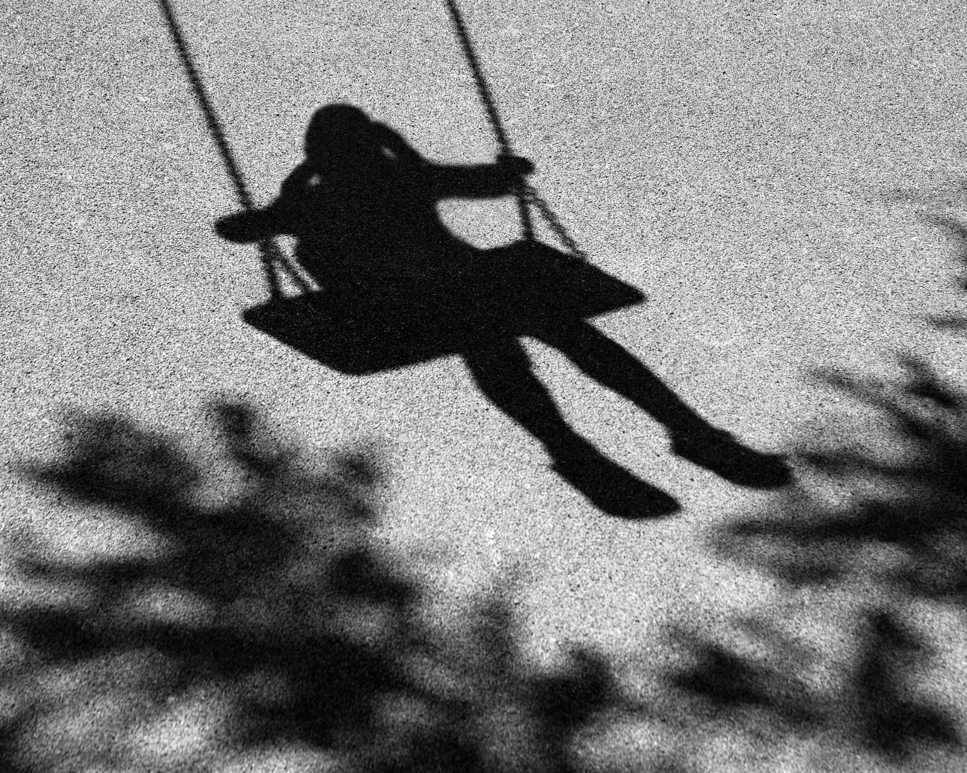 Blurry, black and white shadow of a girl swinging on a swing that is attached to a tree branch