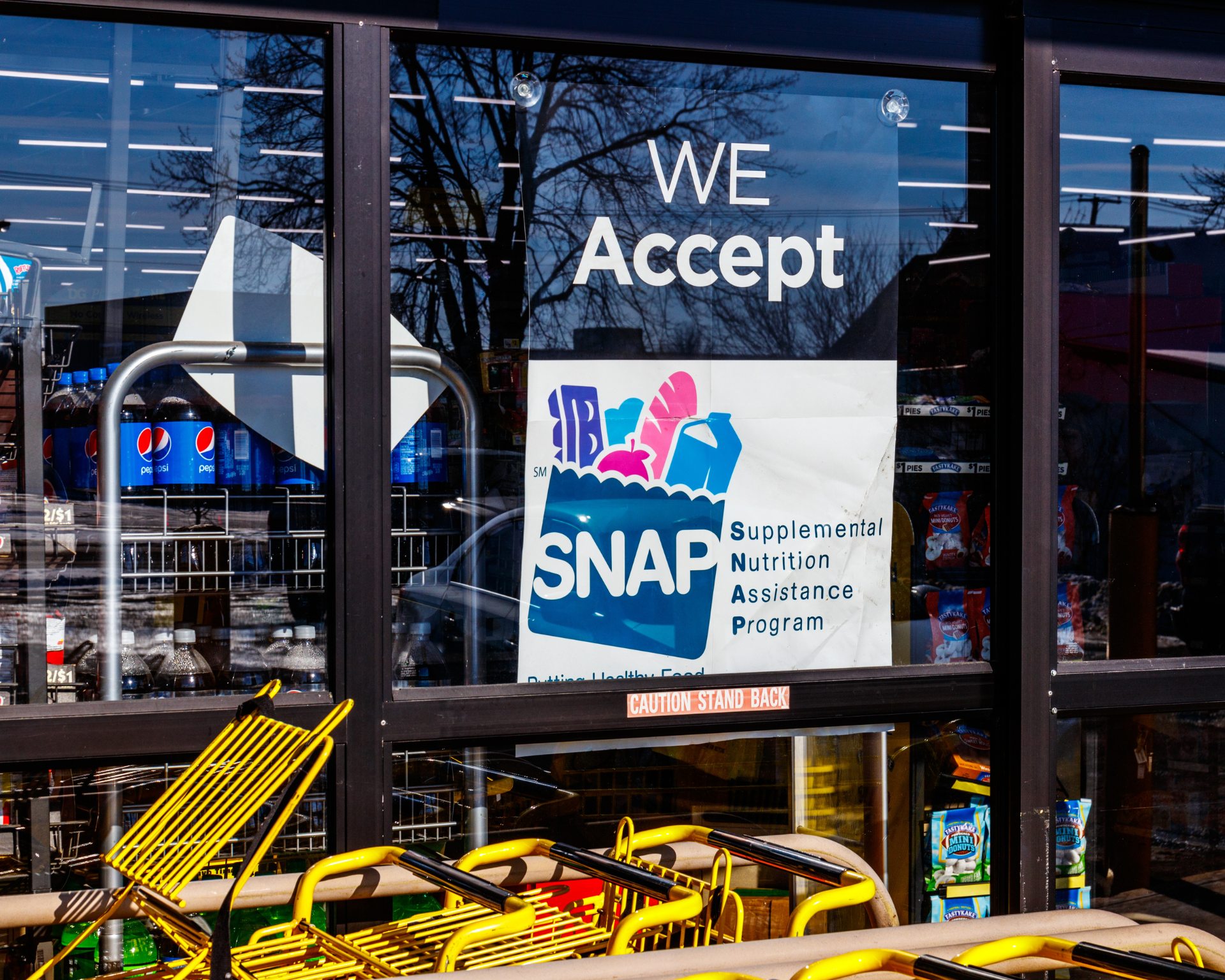 "We Accept SNAP" sign in window of grocery store with yellow grocery carts out front