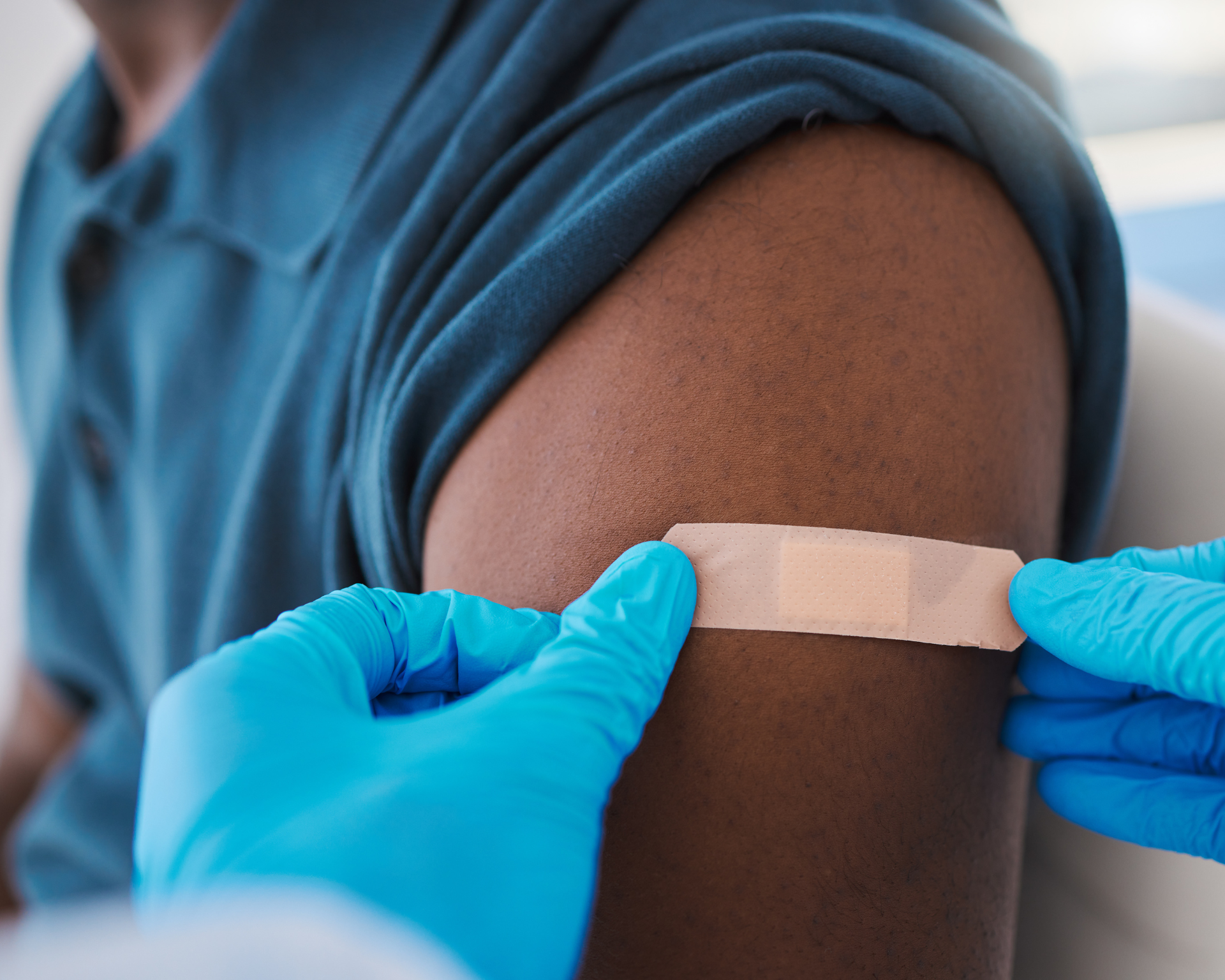 Close-up of a young, healthy male's arm with a bandage after a vaccine shot from a medical professional.