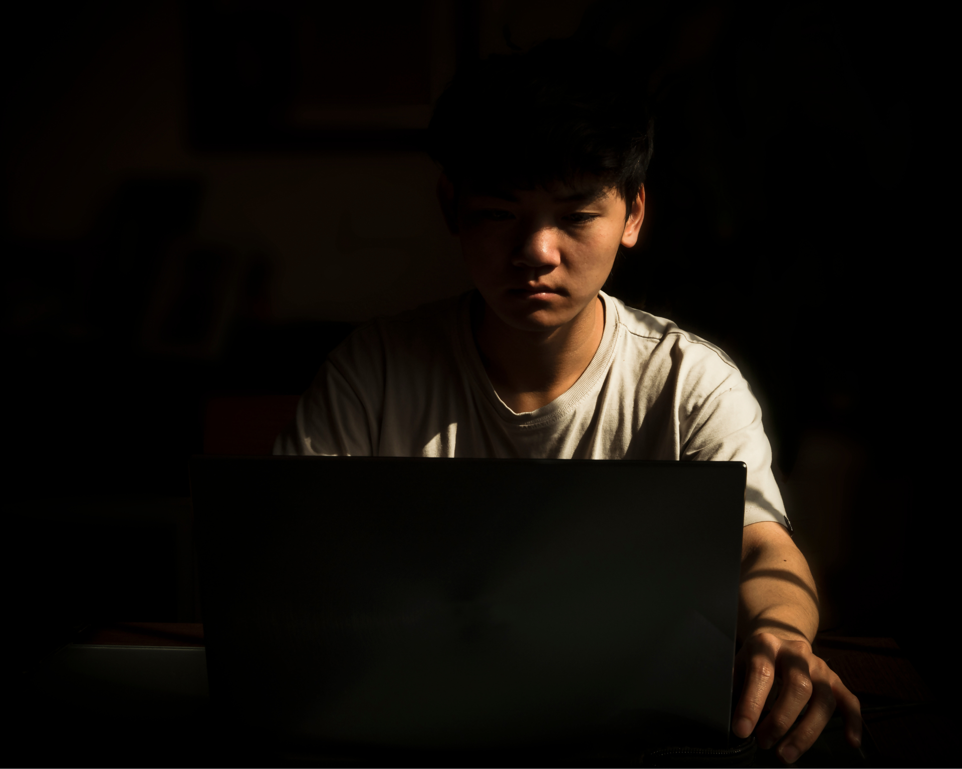 Portrait of teenage Asian boy using laptop indoor with sunlight and shadow