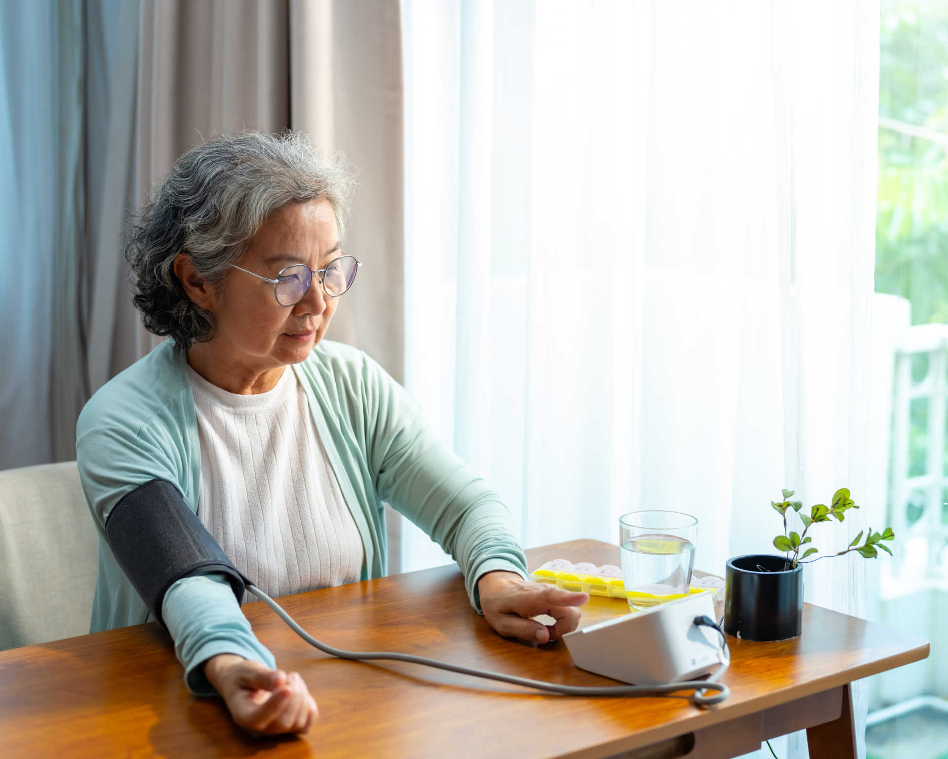 Portrait of a mature Asian woman patient using a remote monitoring tool to measure her blood pressure by herself in her bedroom at home