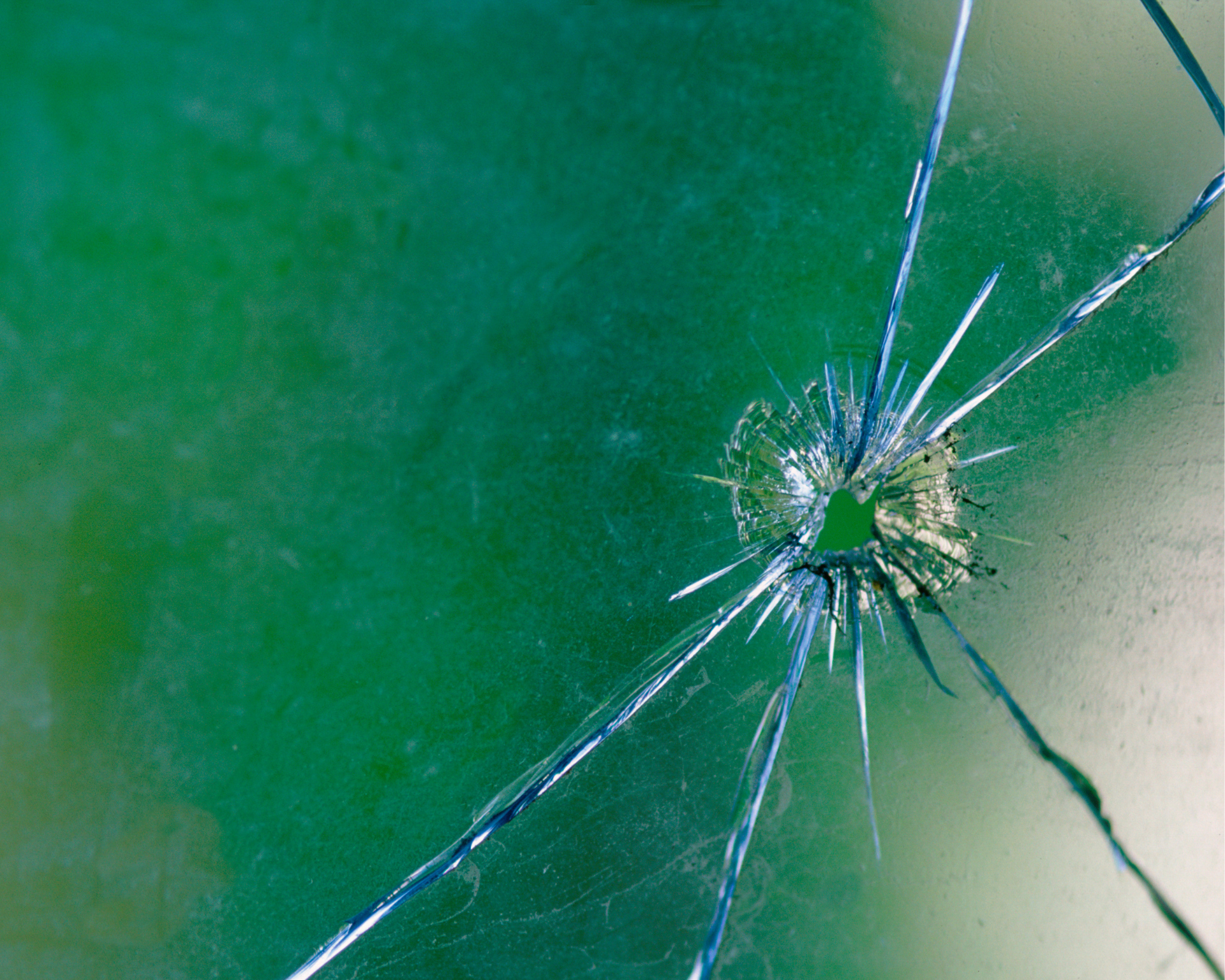 bullet hole in glass with a green and blue background