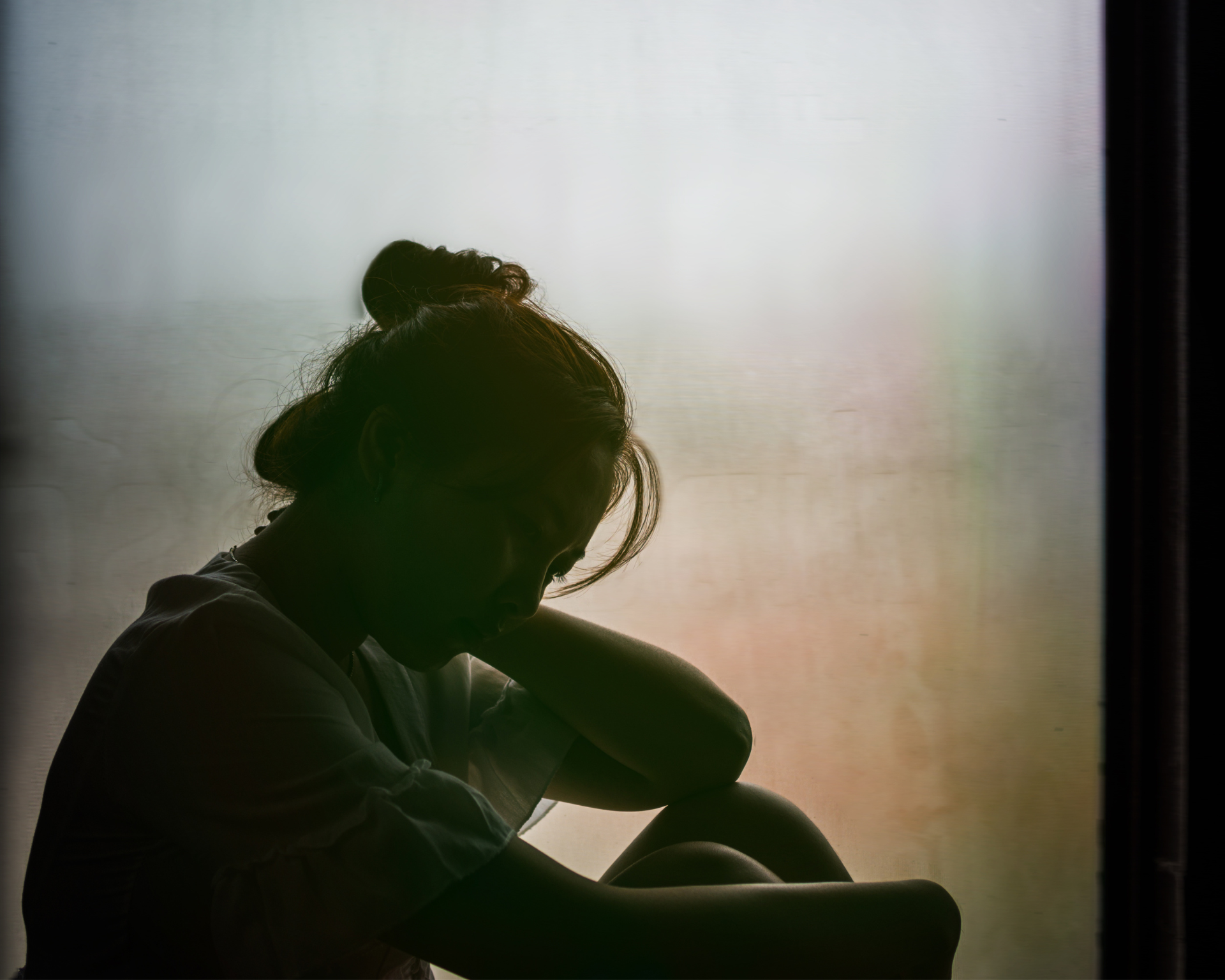 Vintage filter on the silhouette of a sad, young girl sitting near the window. Foster care concept