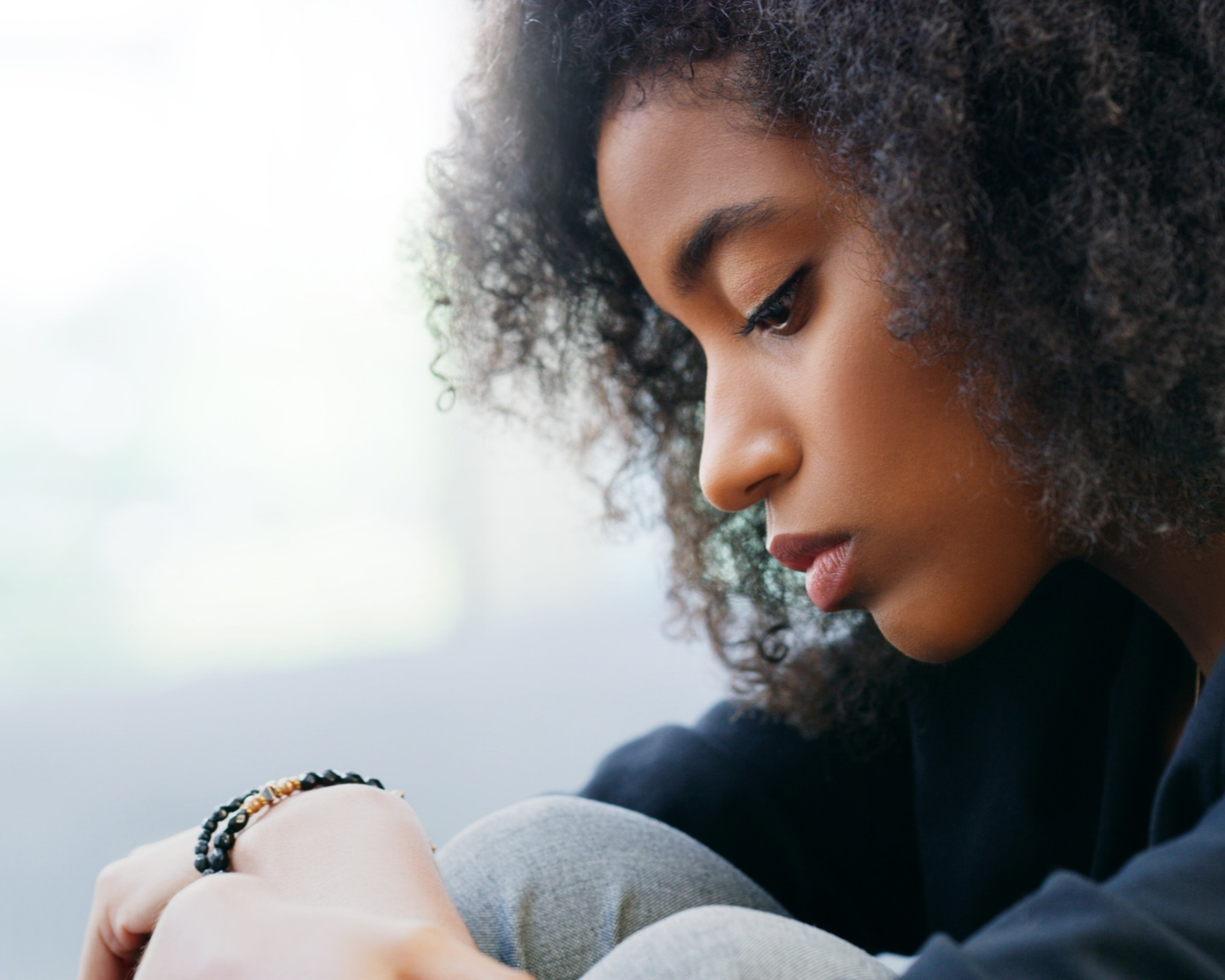 close-up portrait of a young woman looking down at knees. trauma and survivor concept