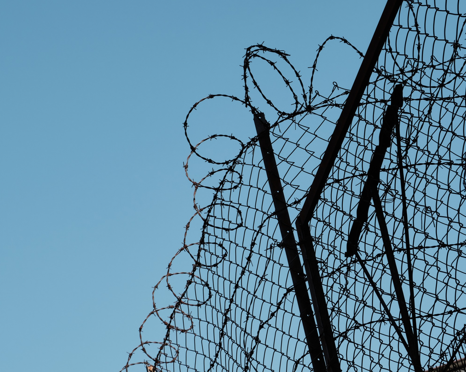 Barbed wire security fence silhouetted against a clear blue sky. Concept of incarceration, imprisonment, freedom