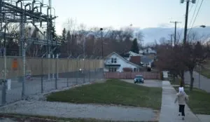 A young child running down a street in Flint, MI, past an electric transformer station