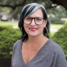a woman with blue hair and glasses smiling