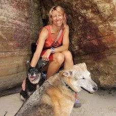 a woman sitting in a cave with two dogs