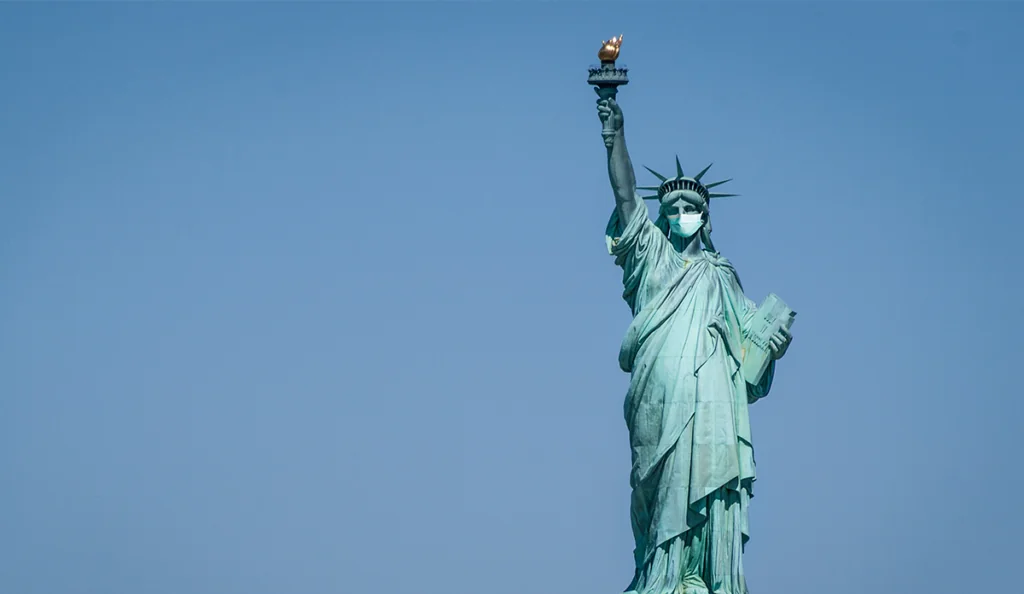 a statue of liberty wearing a face mask with Statue of Liberty in the background
