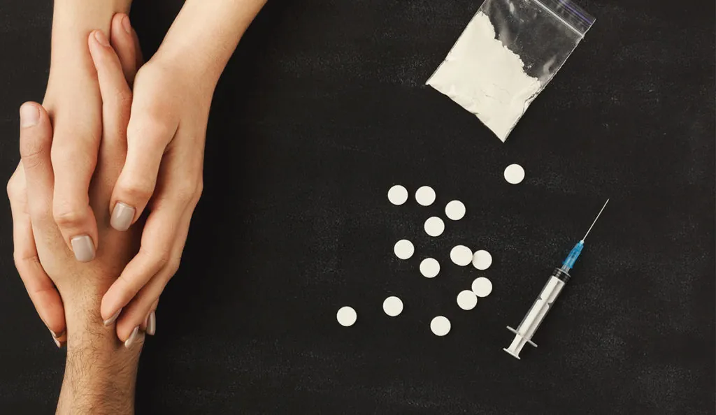 a hand holding a syringe next to a bag of white powder