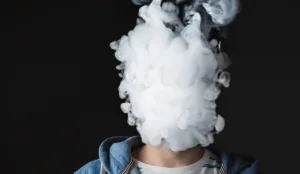 young man with smoke in front of his face, implying youth vaping