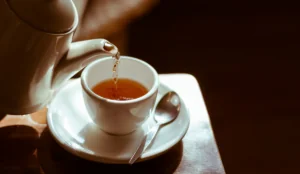 Pouring hot tea into white ceramic tea cup sitting on a saucer