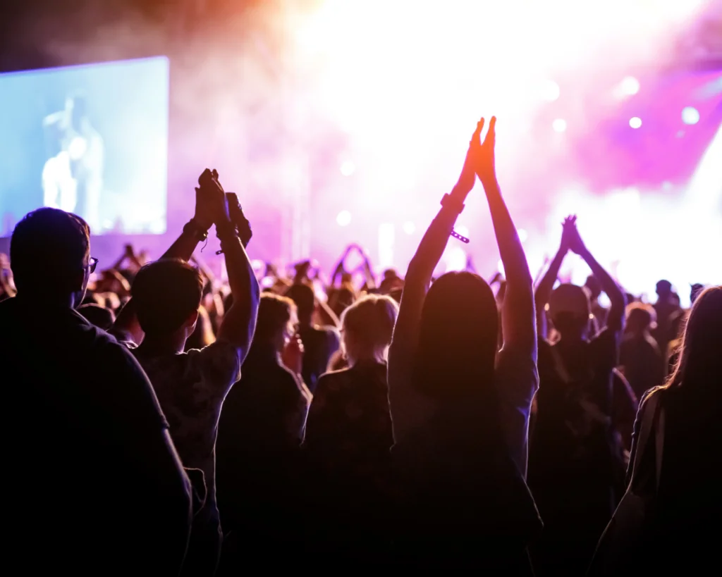 People with raised hands, silhouettes of concert crowd in front of bright stage lights